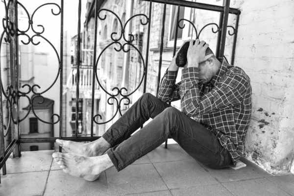 Man with PTSD sitting on the ground outside with his hands covering his face