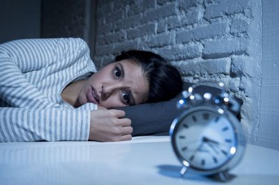 Female fire fighter laying awake in bed at night looking at a clock