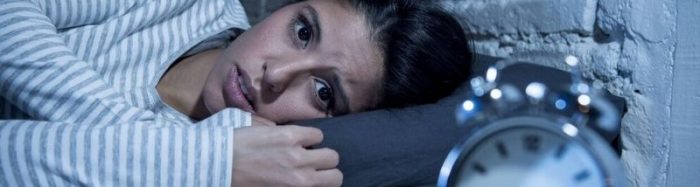 Female fire fighter laying awake at night looking fearfully at the clock