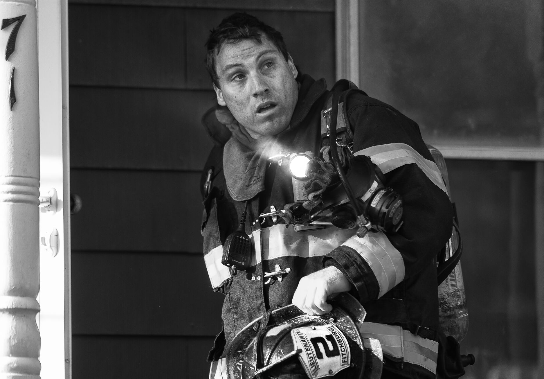 A black and white image of a firefighter leaving a house.
