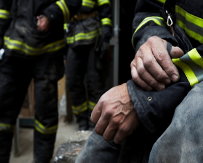 Fire fighter struggling with opioid addiction holding his arm sitting away from his fellow crew members