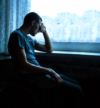man with depression sitting next to window with hand on head