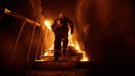 Fire fighter walking up a flight of stairs that are on fire