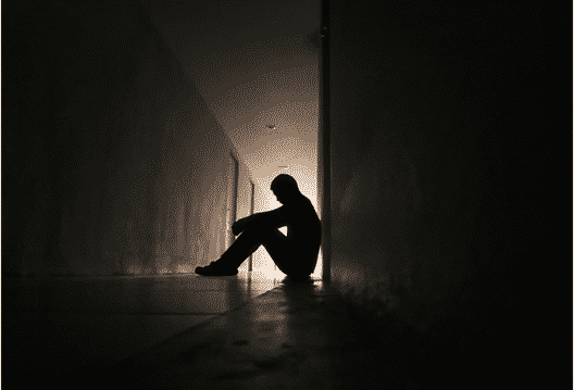 Depressed fire fighter sitting on the ground in a dark outdoor hallway