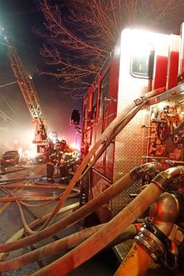 A group of firefighters talking towards the back of a fire truck on the scene