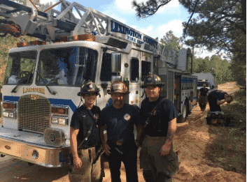 Bill Allenbaugh with a couple of fellow crew members in front of a fire truck in a forest area