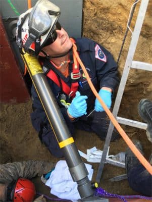 First responder in a hole helping people out smiling up at a person talking