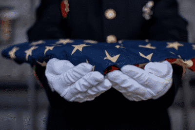 Fire fighter wearing white gloves carrying a folded american flag